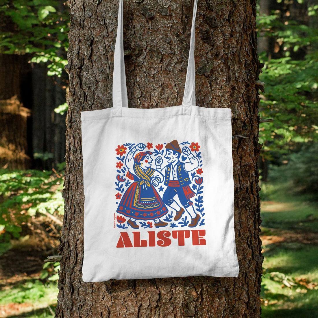 Bolsa de tela cruda con la ilustración de la pareja alistana impresa al frente, colgada de la rama de un pino, vista cuadrada