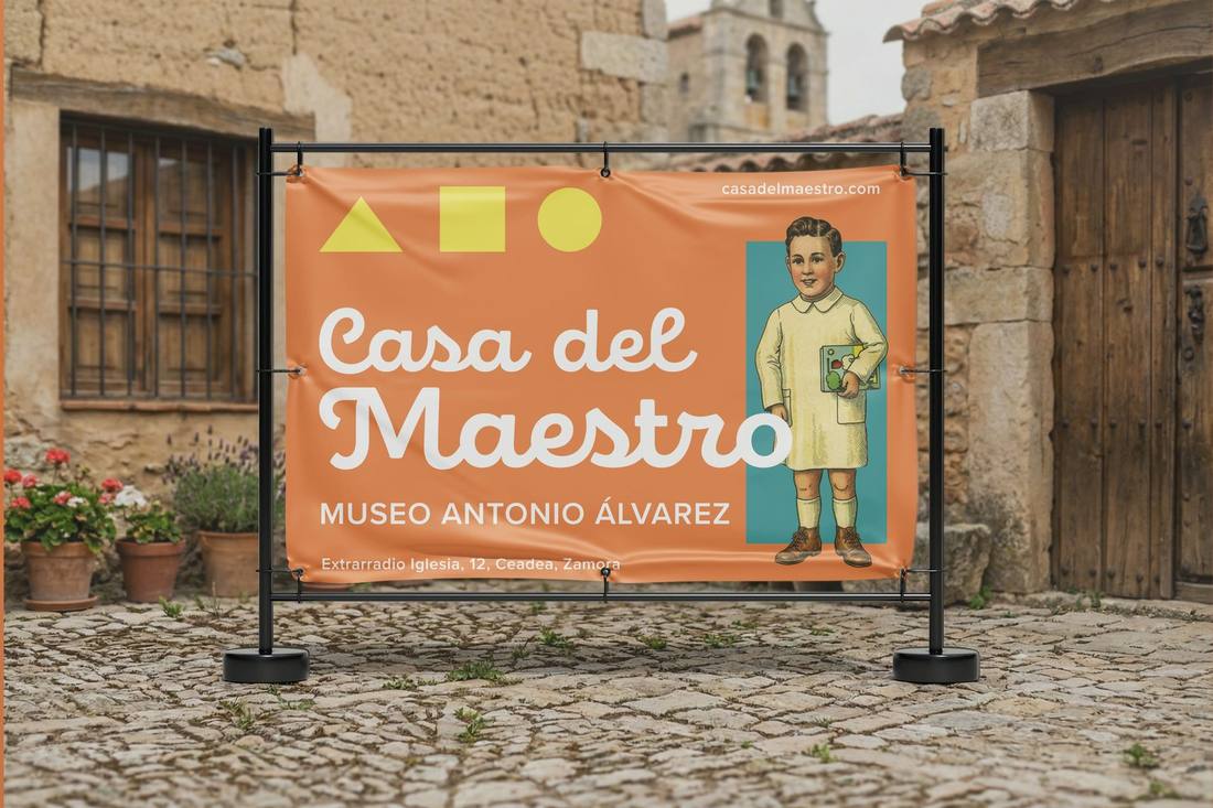 Lona horizontal de gran formato en estructura metálica negra, instalada en el patio empedrado de un edificio de piedra del pueblo, con cabecera «Casa del Maestro» en cursiva blanca, descriptor del museo, dirección «Extrarradio Iglesia, 12, Ceadea, Zamora» y niño ilustrado con cuaderno