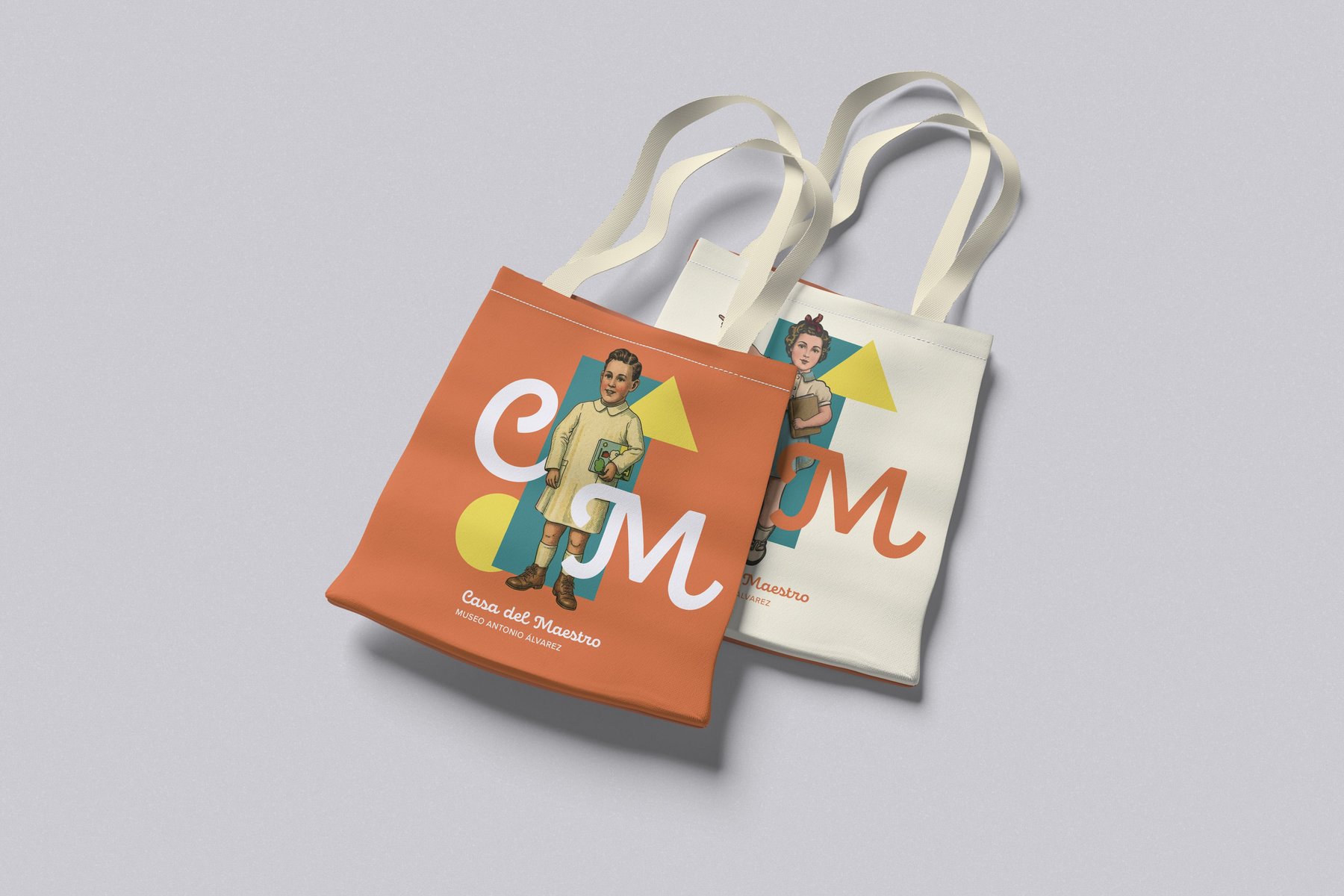 Dos tote bags de algodón apilados —una en naranja con niño, otra en blanco crema con niña— ambas con monograma CM y lockup del museo