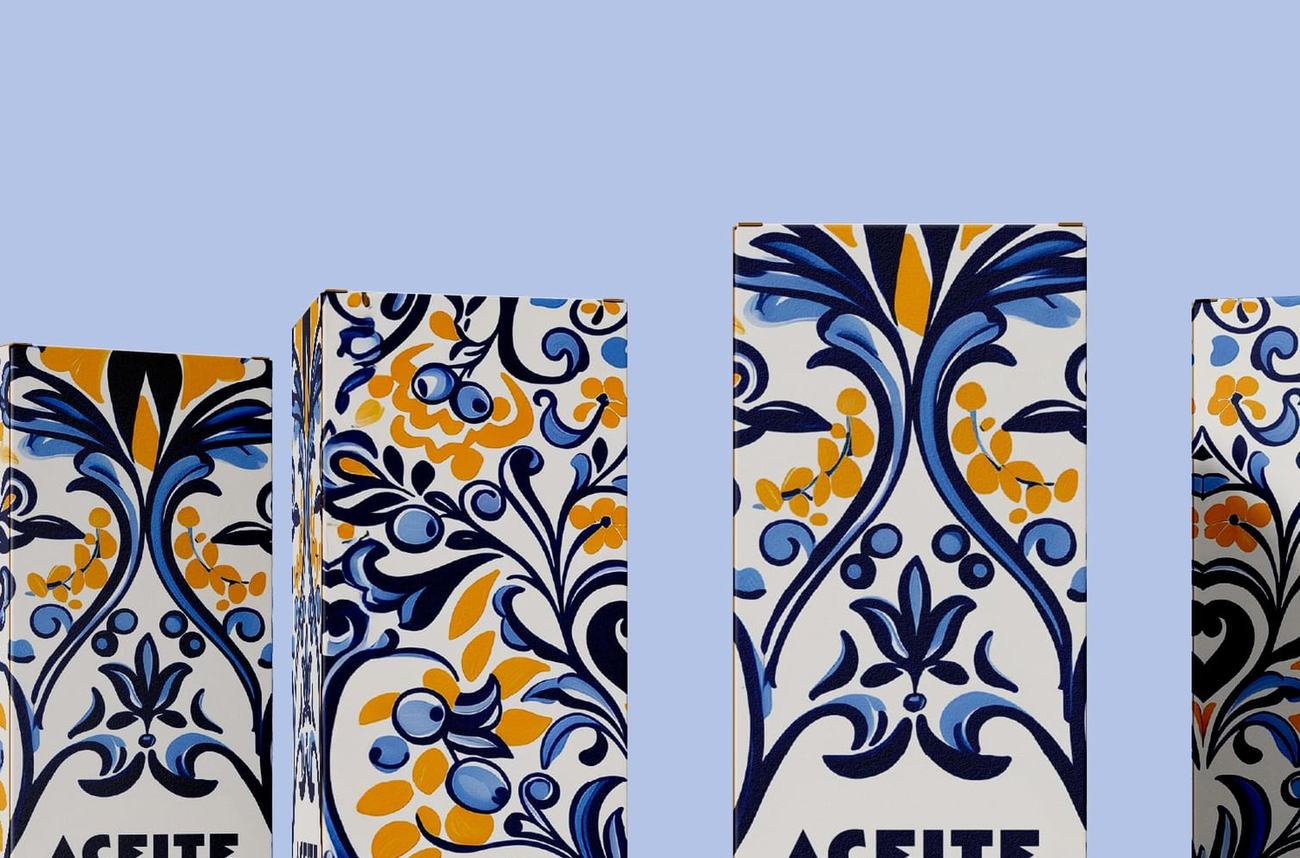 Detalle de las caras frontales de varias cajas de Oleotoledo, con el patrón cerámico aplicado en azul cobalto y amarillo dorado sobre blanco, sobre fondo lila pálido