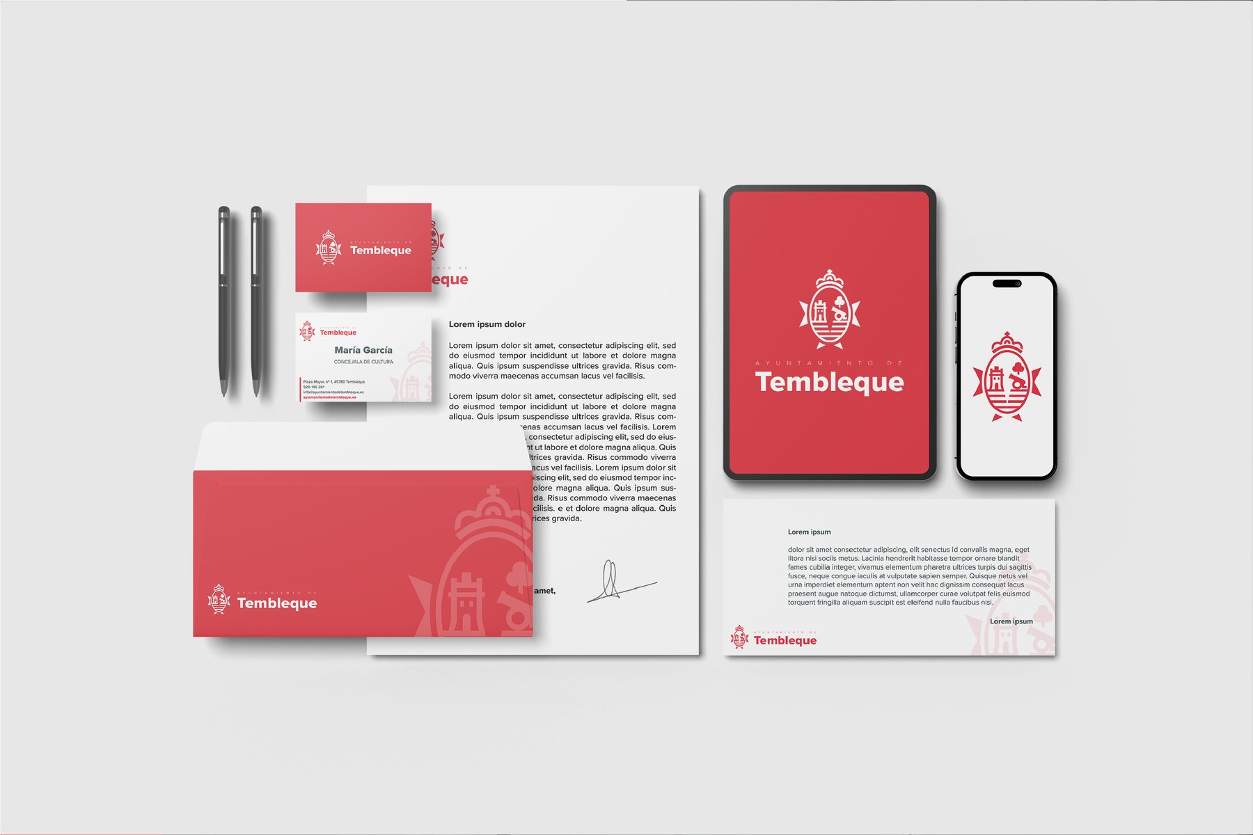 Escaparate del sistema integral: tarjetas de visita, sobres, hojas membretadas, tablet y móvil mostrando la web institucional, todo con la marca aplicada en rojo
