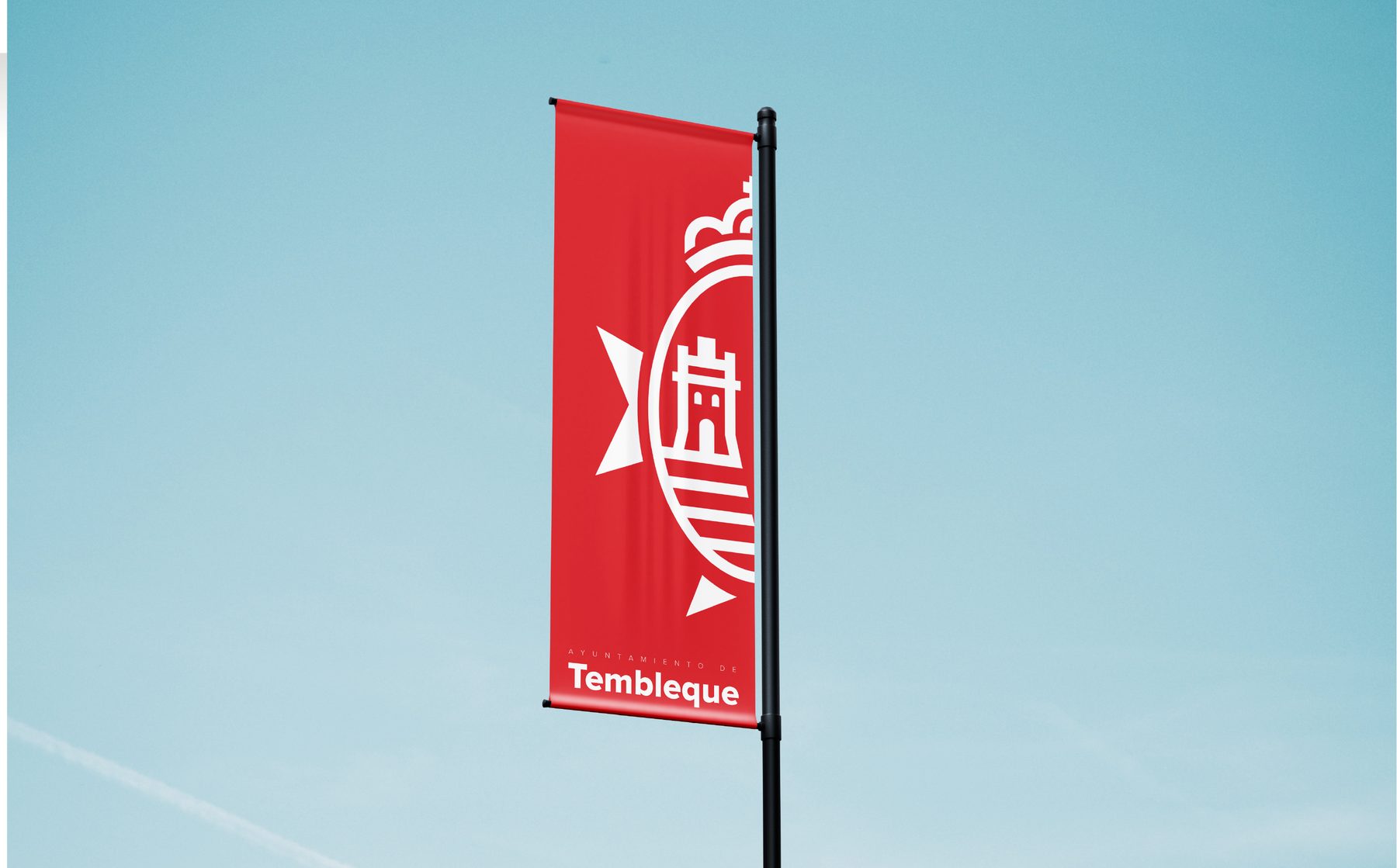 Bandera vertical roja con escudo blanco grande, ondeando contra cielo azul