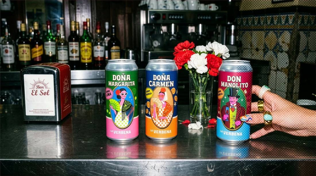 Tres latas de La Verbena alineadas en la barra de un bar tradicional con botellería detrás y claveles rojos a los lados